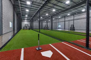 Row of batting cages with netting and turf inside a baseball training facility