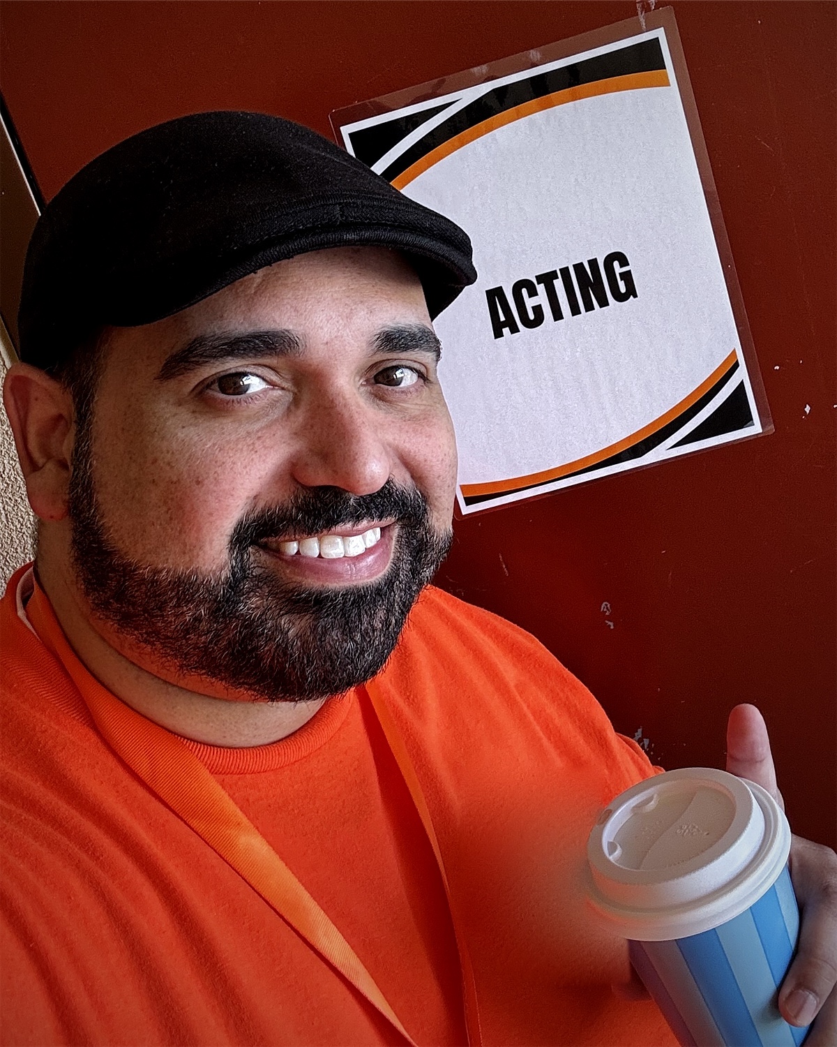 Robert Amaya smiling with a coffee outside a classroom door marked Acting