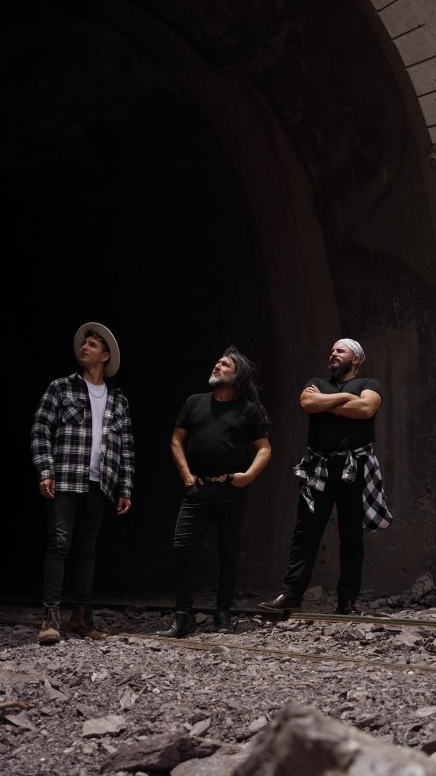 Los tres integrantes de Los Oviedo dentro de un túnel de piedra, mirando hacia arriba