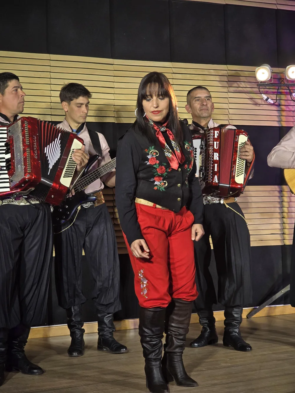 Tiana en el escenario con su chaleco bordado y pantalón rojo, junto a los músicos