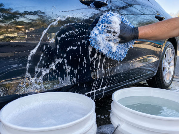 Hand wash with two bucket method on car panel during full exterior detail