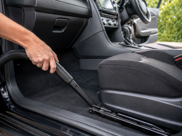 Interior detail vacuuming carpet and seat track of vehicle during full auto detail