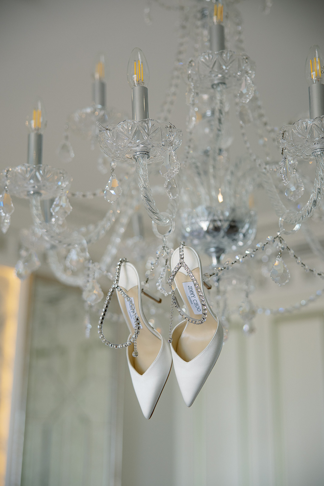 Luxury Jimmy Choo bridal shoes hanging from a crystal chandelier during bridal preparations at Raffles The Palm Dubai, photographed in elegant natural light by a Dubai wedding photographer. Luxury Jimmy Choo bridal shoes hanging from a crystal chandelier during bridal preparations at Raffles The Palm Dubai, photographed in elegant natural light by a Dubai wedding photographer.