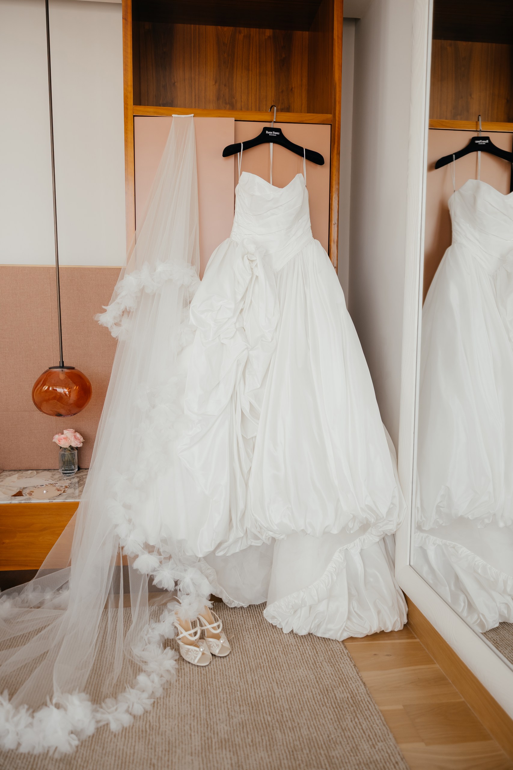 White wedding dress, feather-trimmed veil and bridal shoes beside a mirror at The Lana hotel in Dubai.
