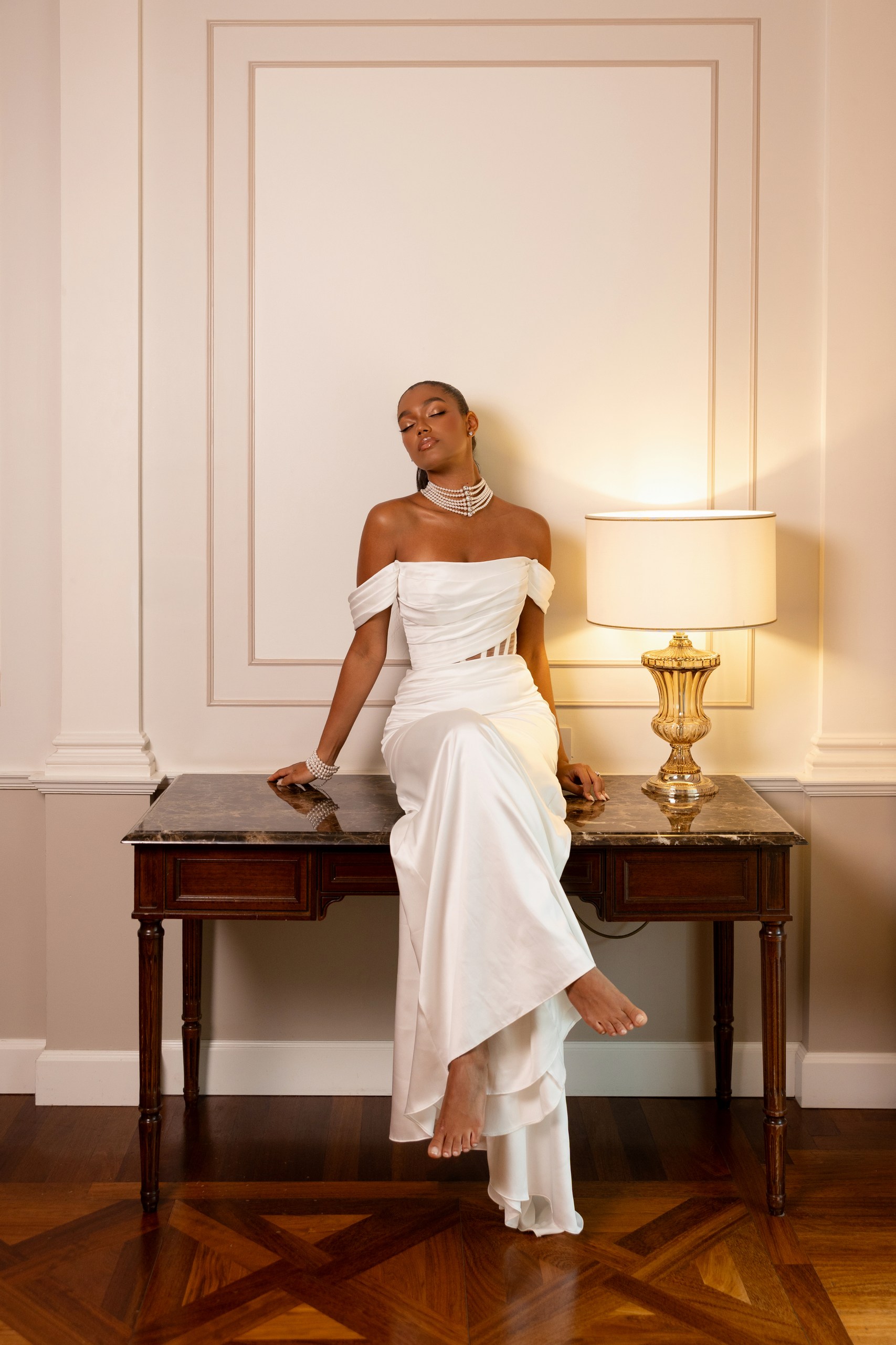 Groom in a black tuxedo holding the bride at her waist as she leans against him in an off-the-shoulder white gown.
