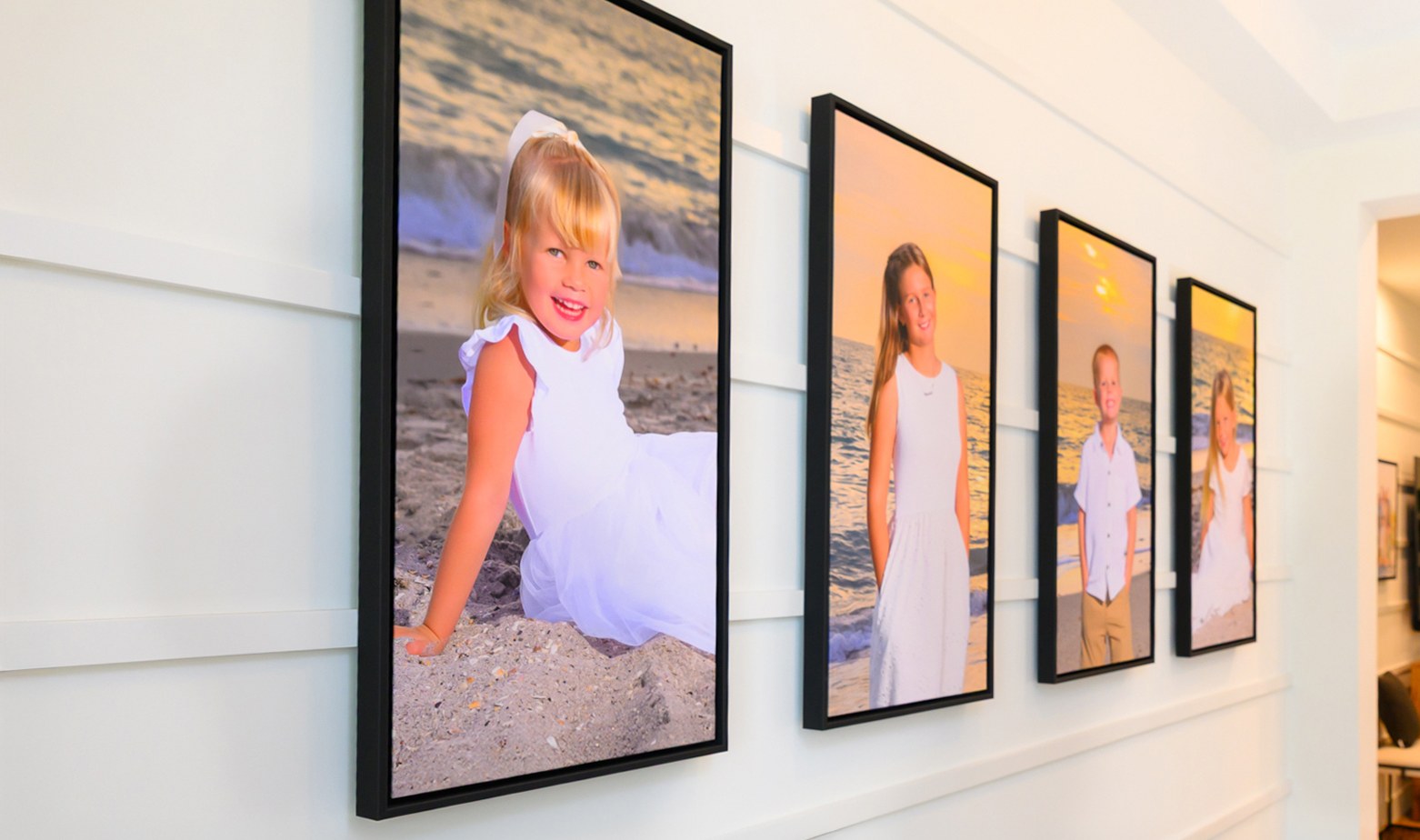 Four large black-framed beach portraits of grandchildren installed on a shiplap wall