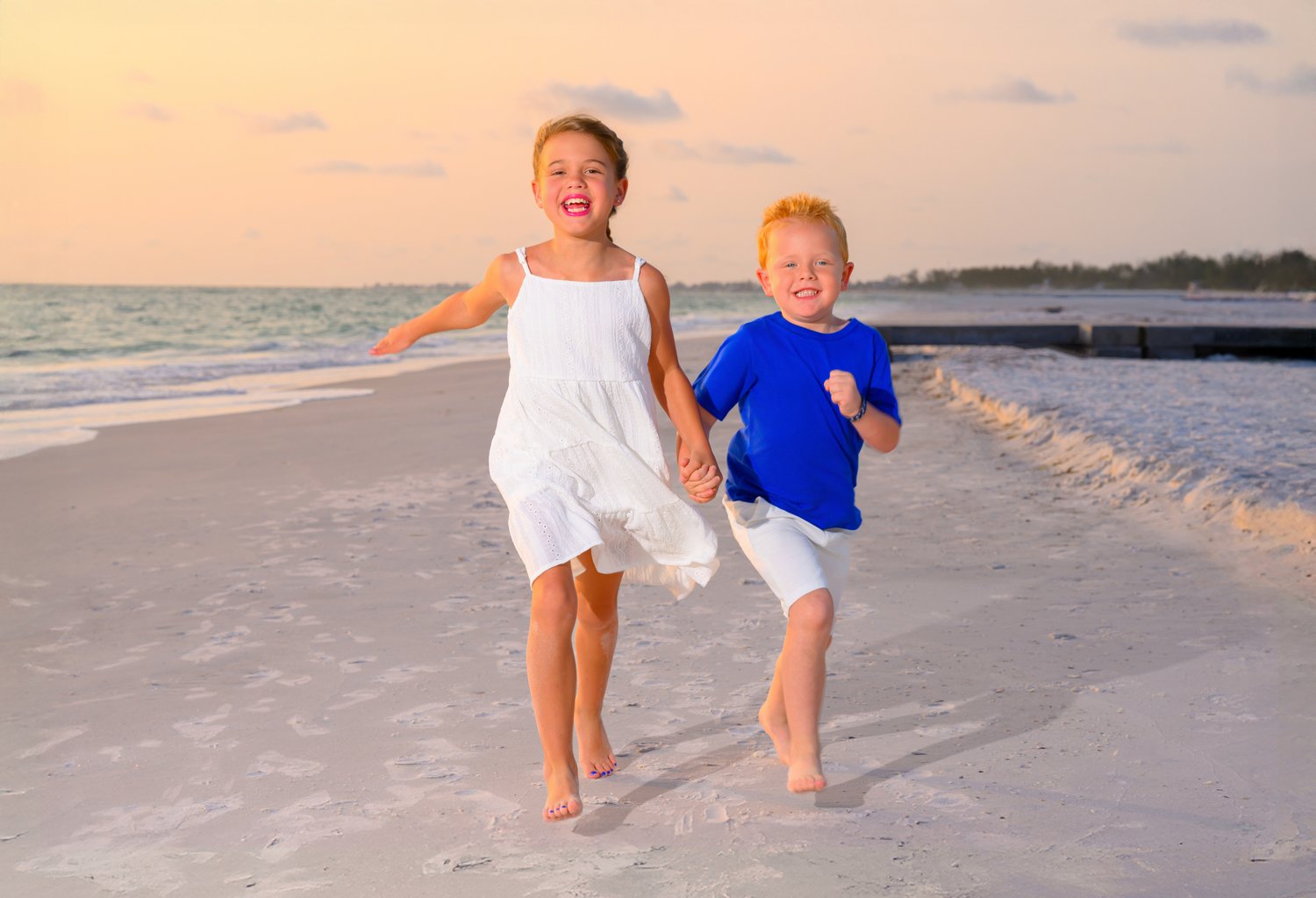 Two children running along the sand at sunset