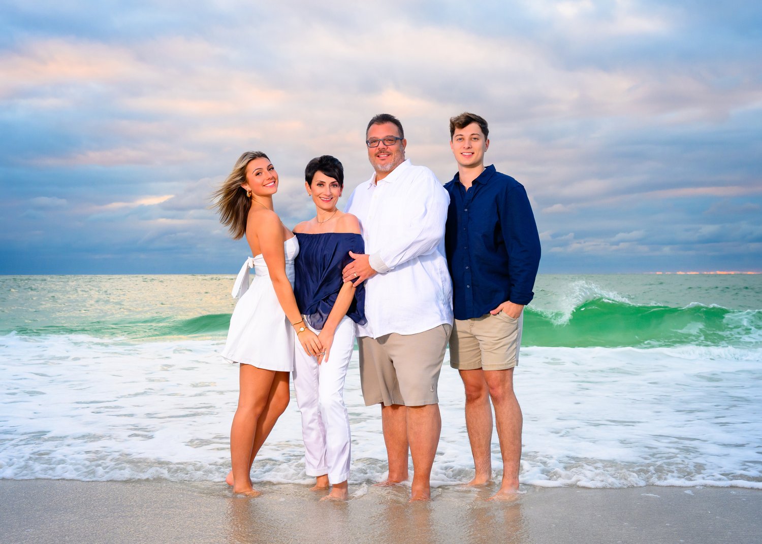 Family of four at the shoreline with a breaking wave behind them