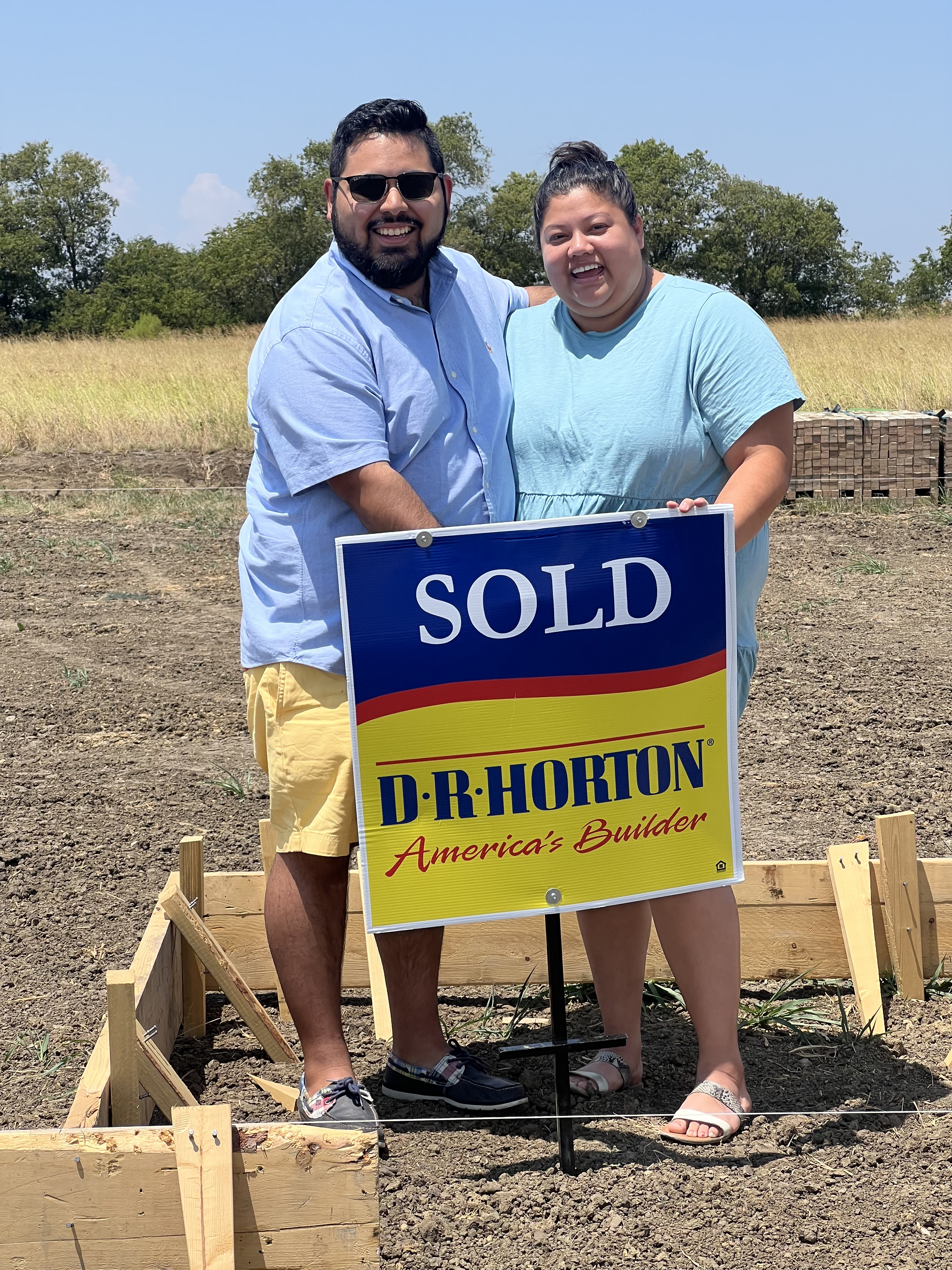 Happy couple holding a sold sign in front of their new DFW home