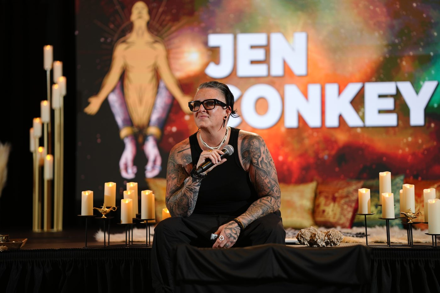 Jen Conkey seated on stage with a microphone, her name on the screen behind her