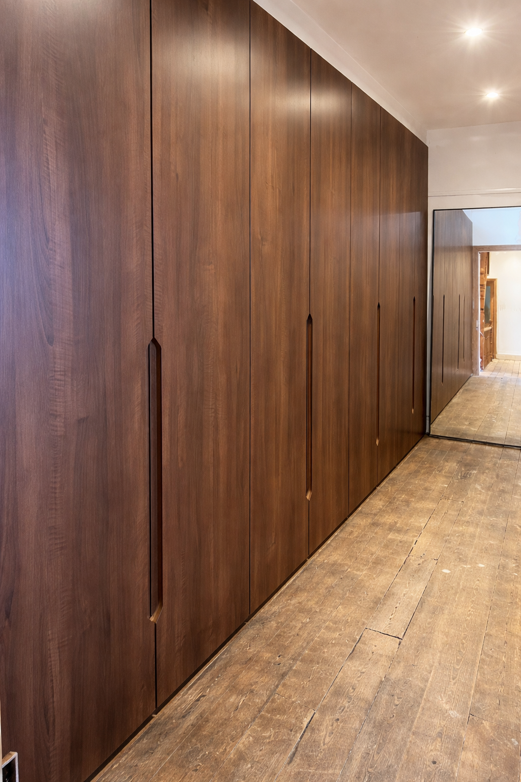 full height walnut fitted wardrobes with integrated handles along hallway bespoke storage design UK