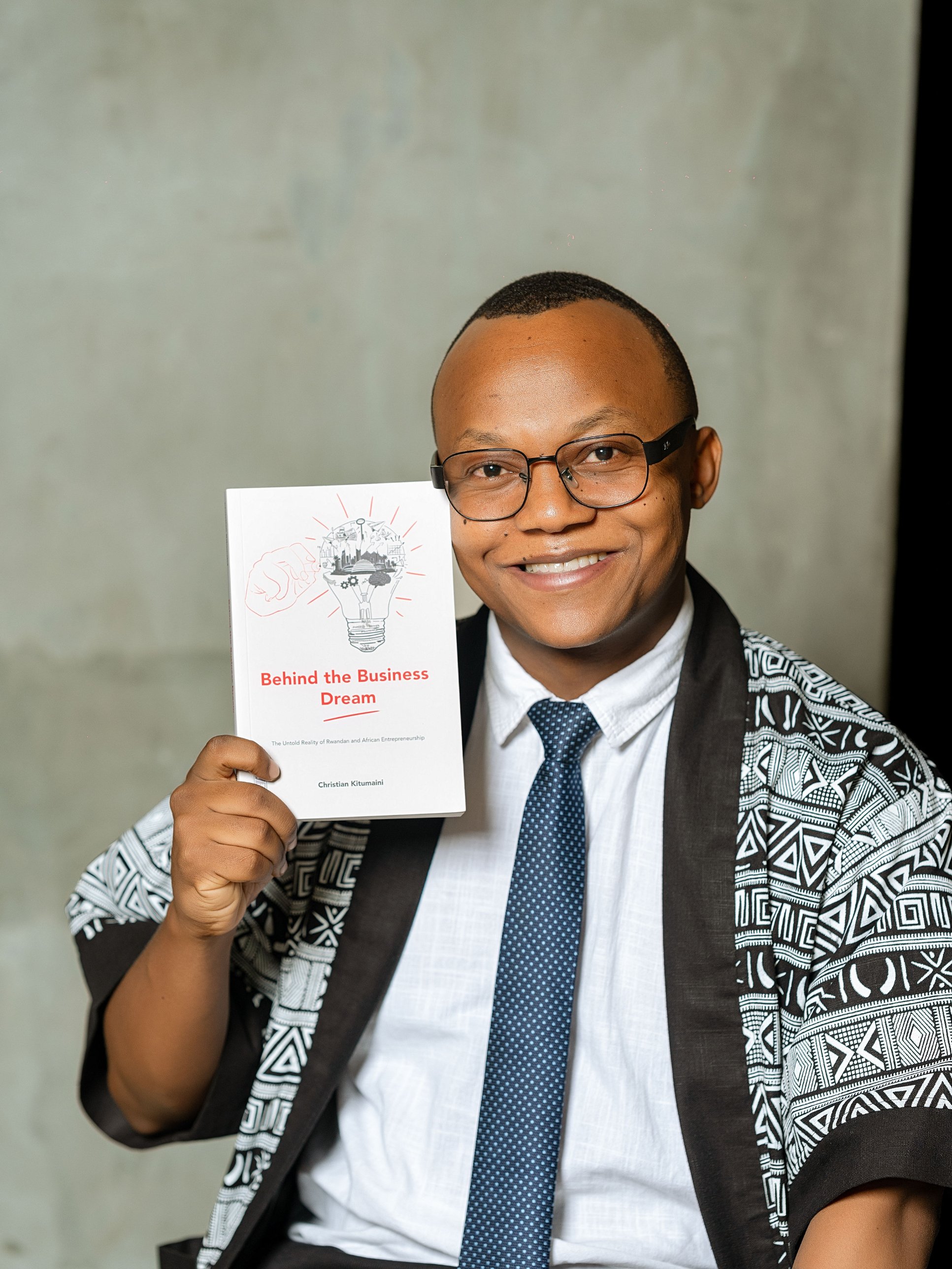Christian Kitumaini smiling and holding a copy of Behind the Business Dream