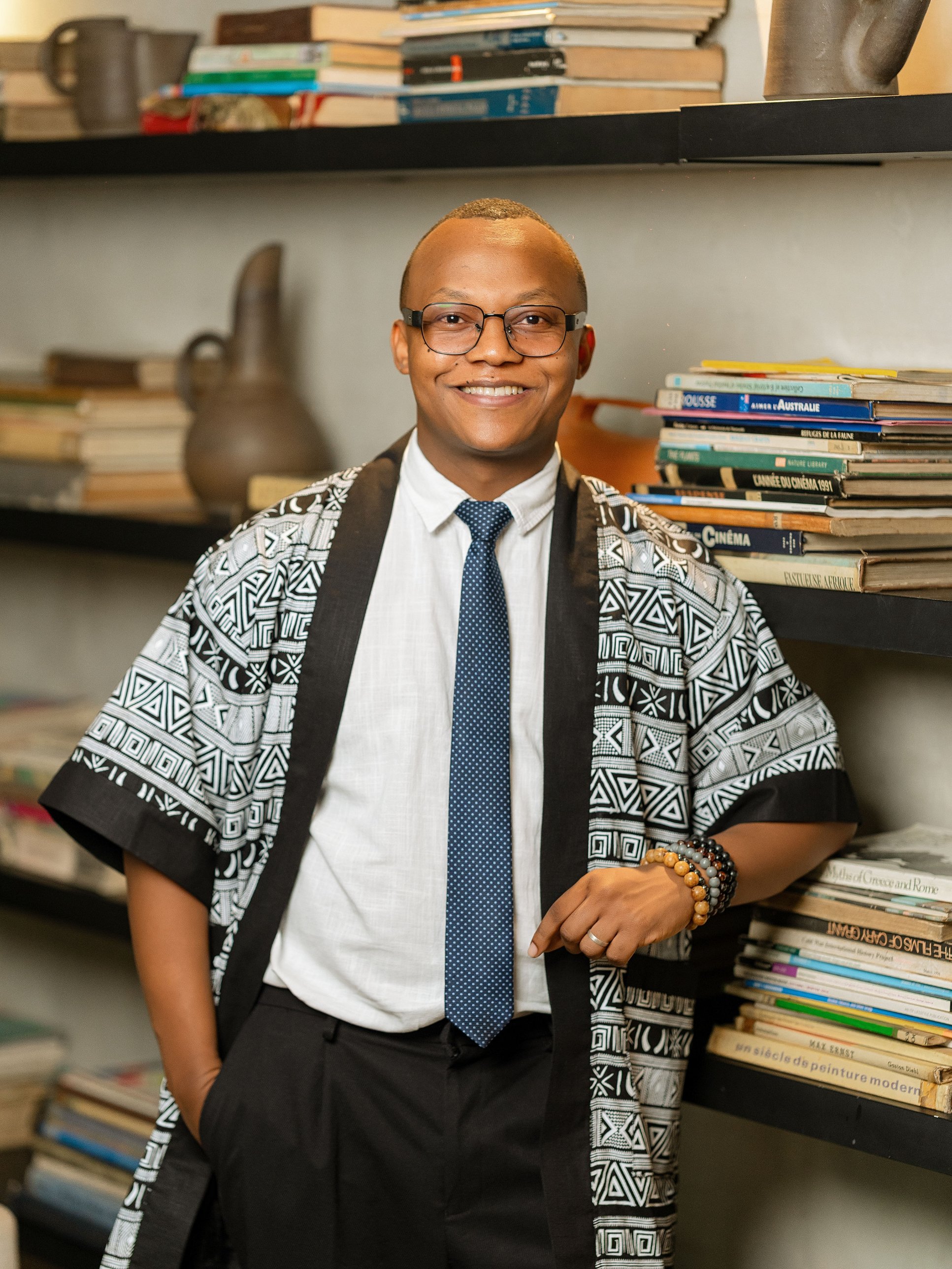 Christian Kitumaini standing beside a bookshelf
