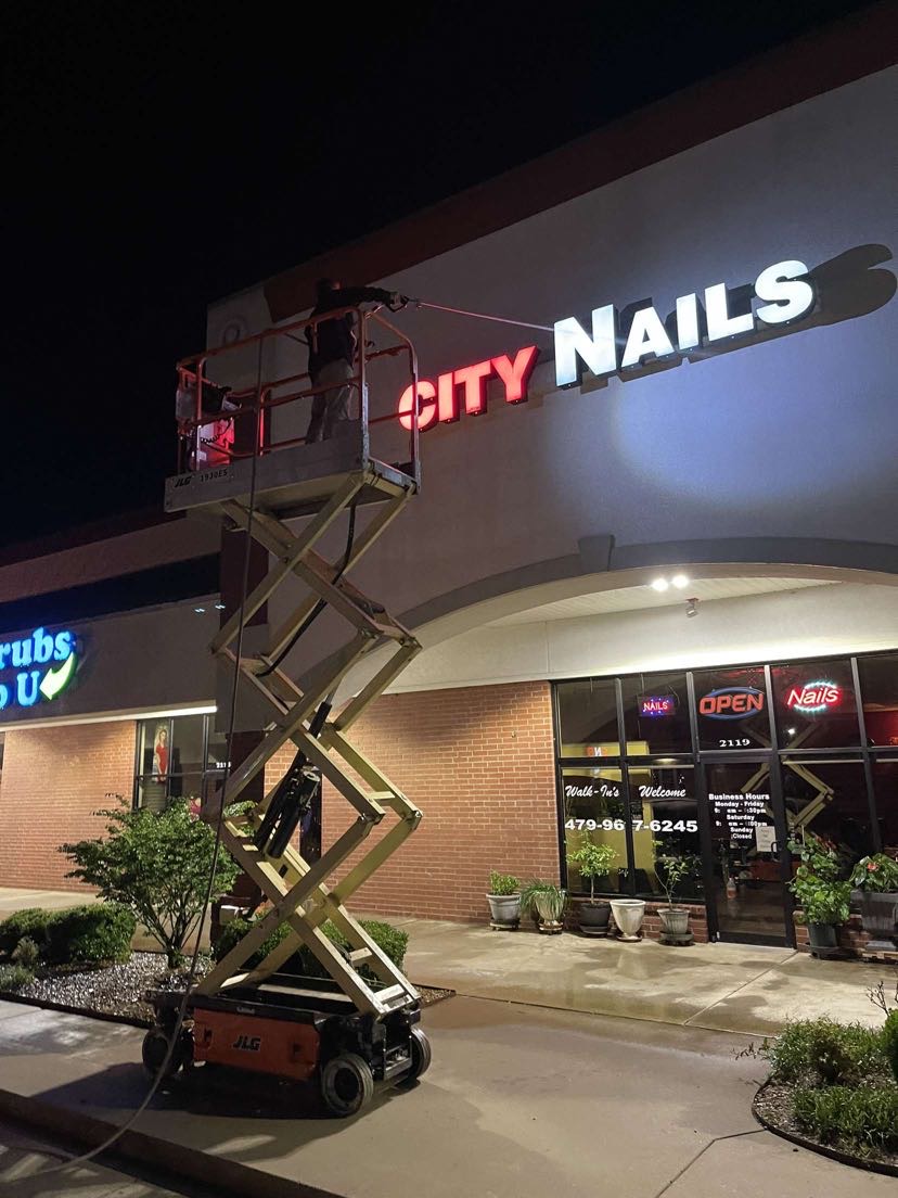 Technician on a lift pressure washing a commercial storefront sign