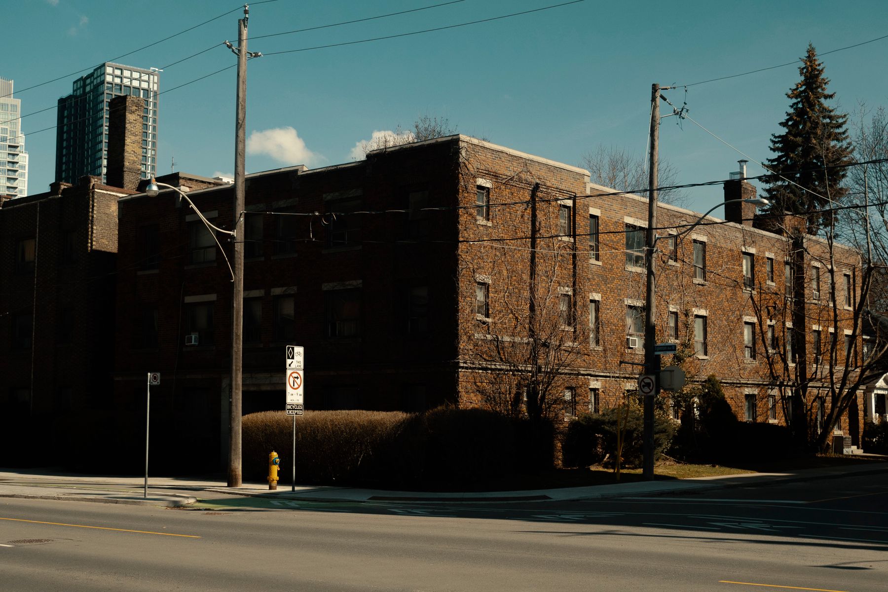 Three-storey brick walk-up apartment on a Toronto street corner with a condo tower behind it