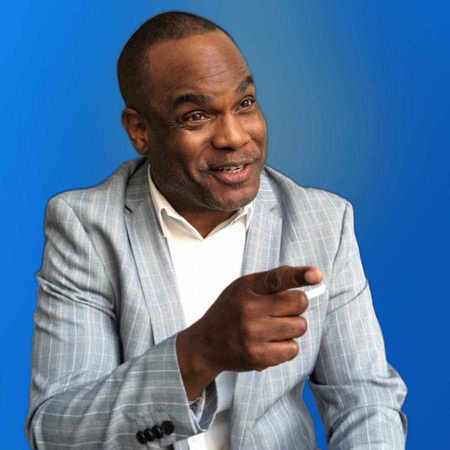 Dwayne Golden pointing toward the camera in a gray plaid jacket