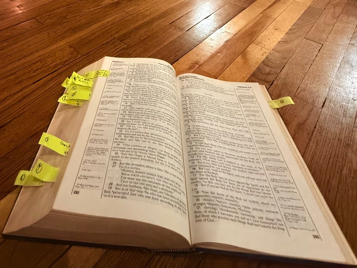 An open, well-used Bible with sticky-note tabs on a wood floor