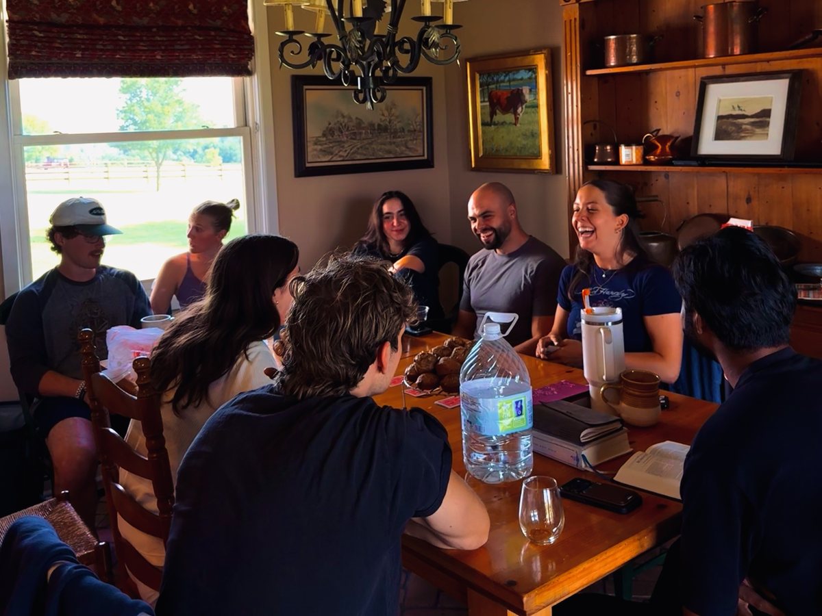 Friends laughing around a farmhouse dinner table