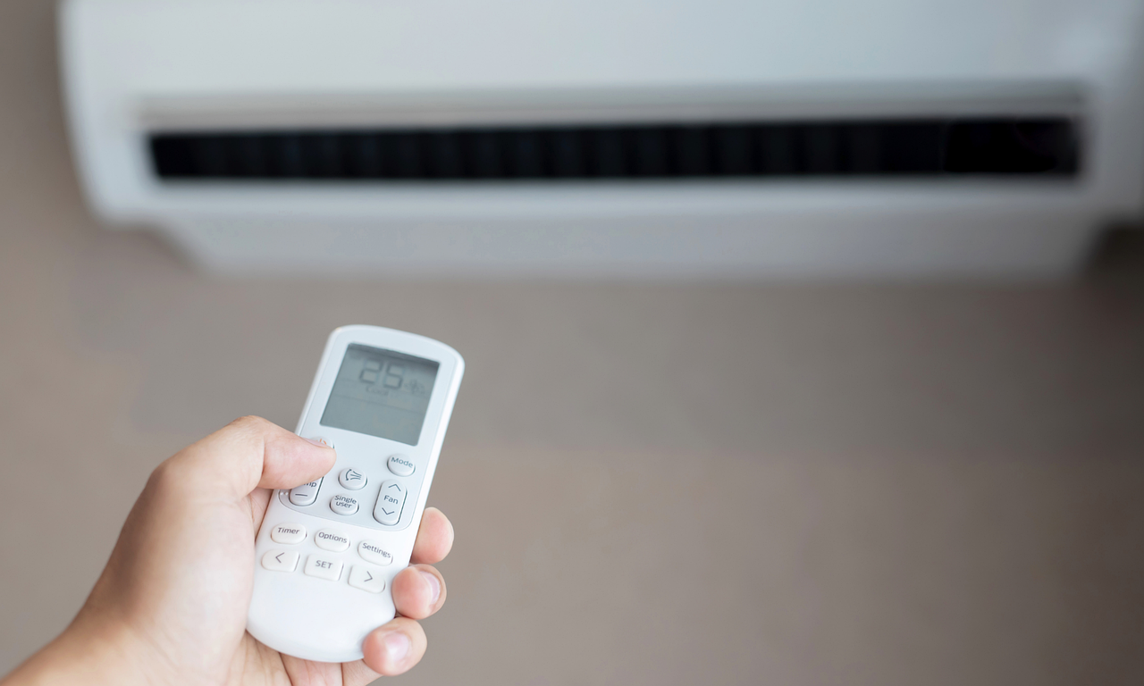 Hand holding an air-conditioning remote to control indoor comfort
