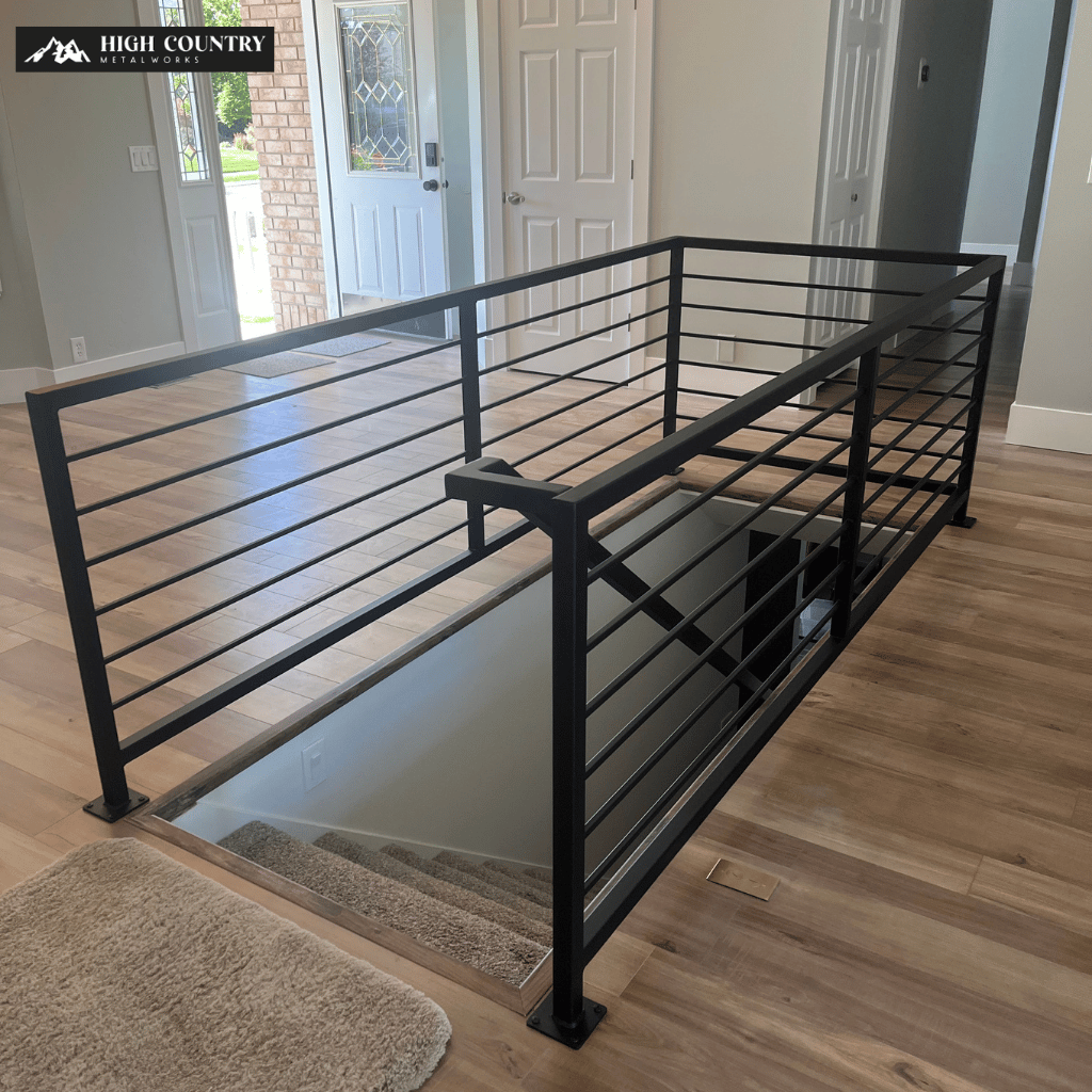 Modern interior with sleek black aluminum railing on stairway, light wood floors, open doorway to sunlit yard.