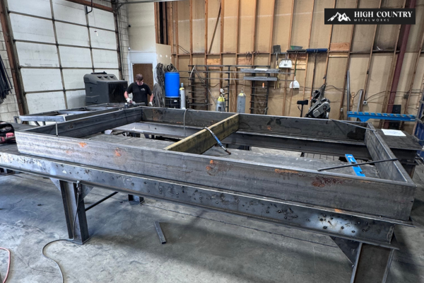 A fabricator fabricates custom steel frames on a large metal table in a workshop for storefront canopies and awnings.