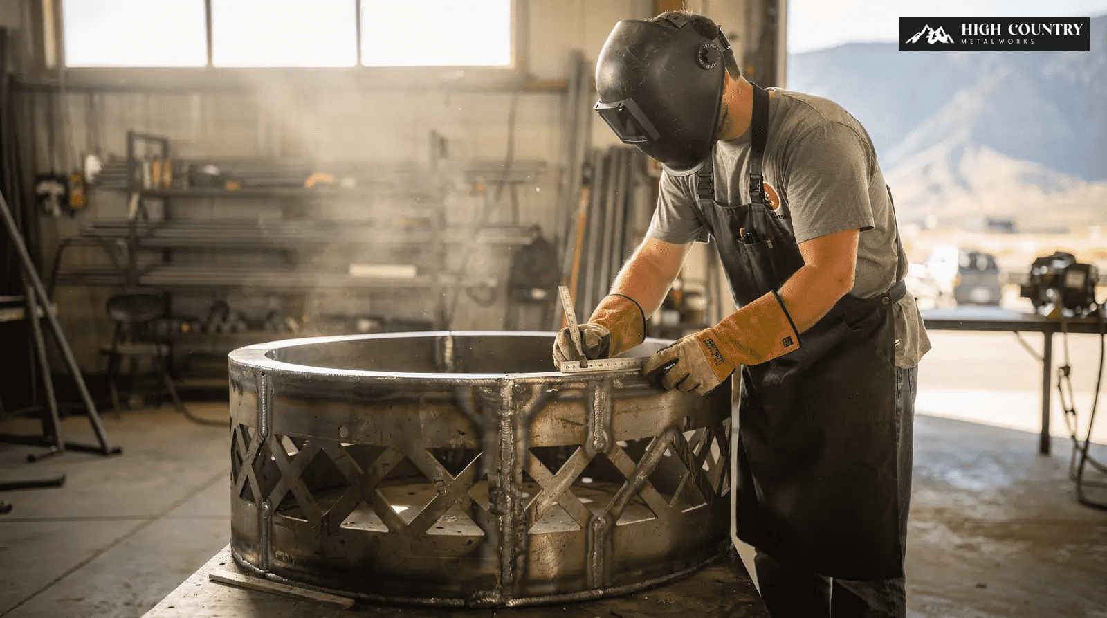 A welder in an apron welds a large metal pot, showcasing the fabrication process of a metal fire pit. A welder in an apron welds a large metal pot, showcasing the fabrication process of a metal fire pit.