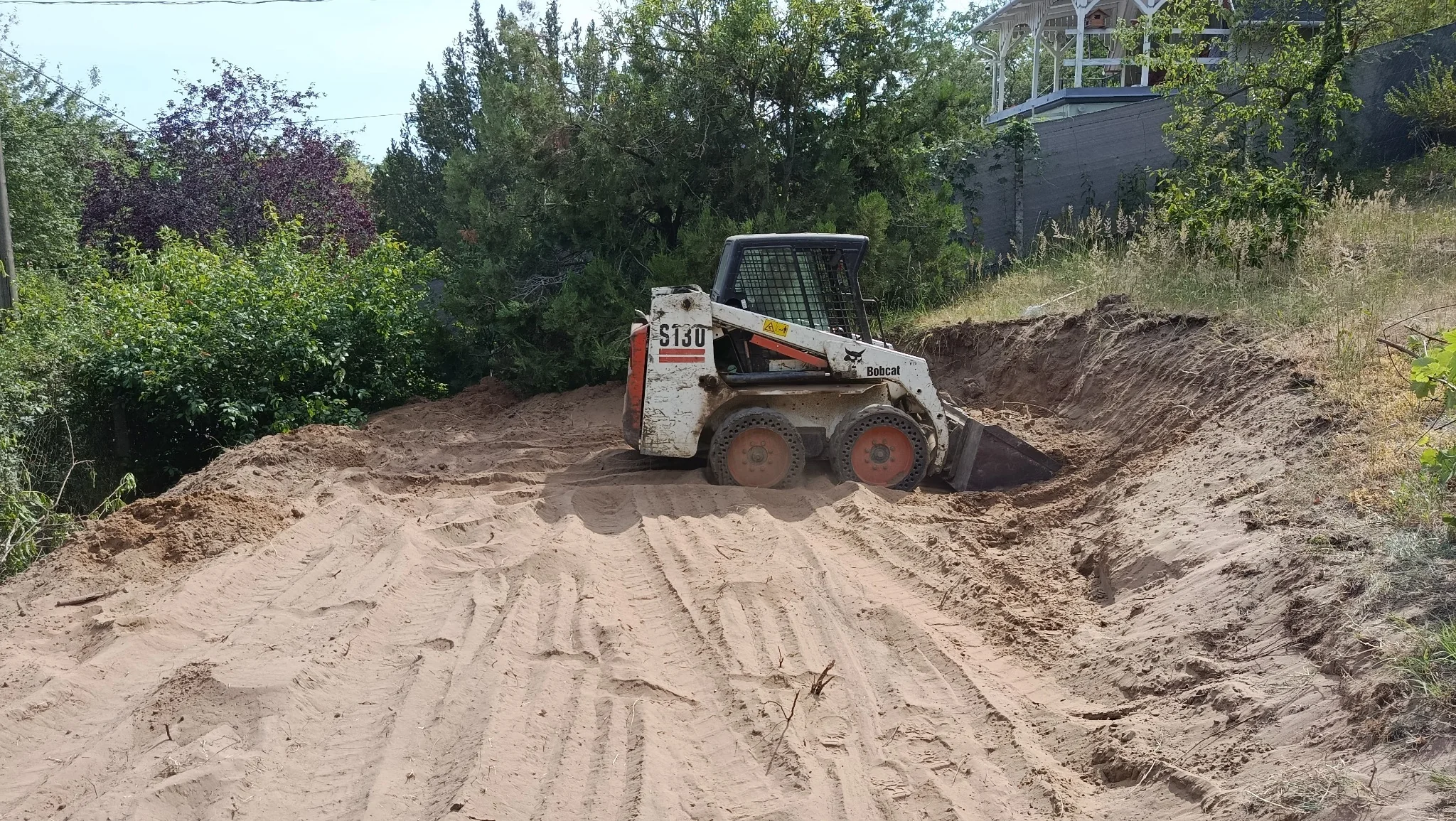 Gépi tereprendezés kompakt rakodógéppel egy kertben – Zsékert