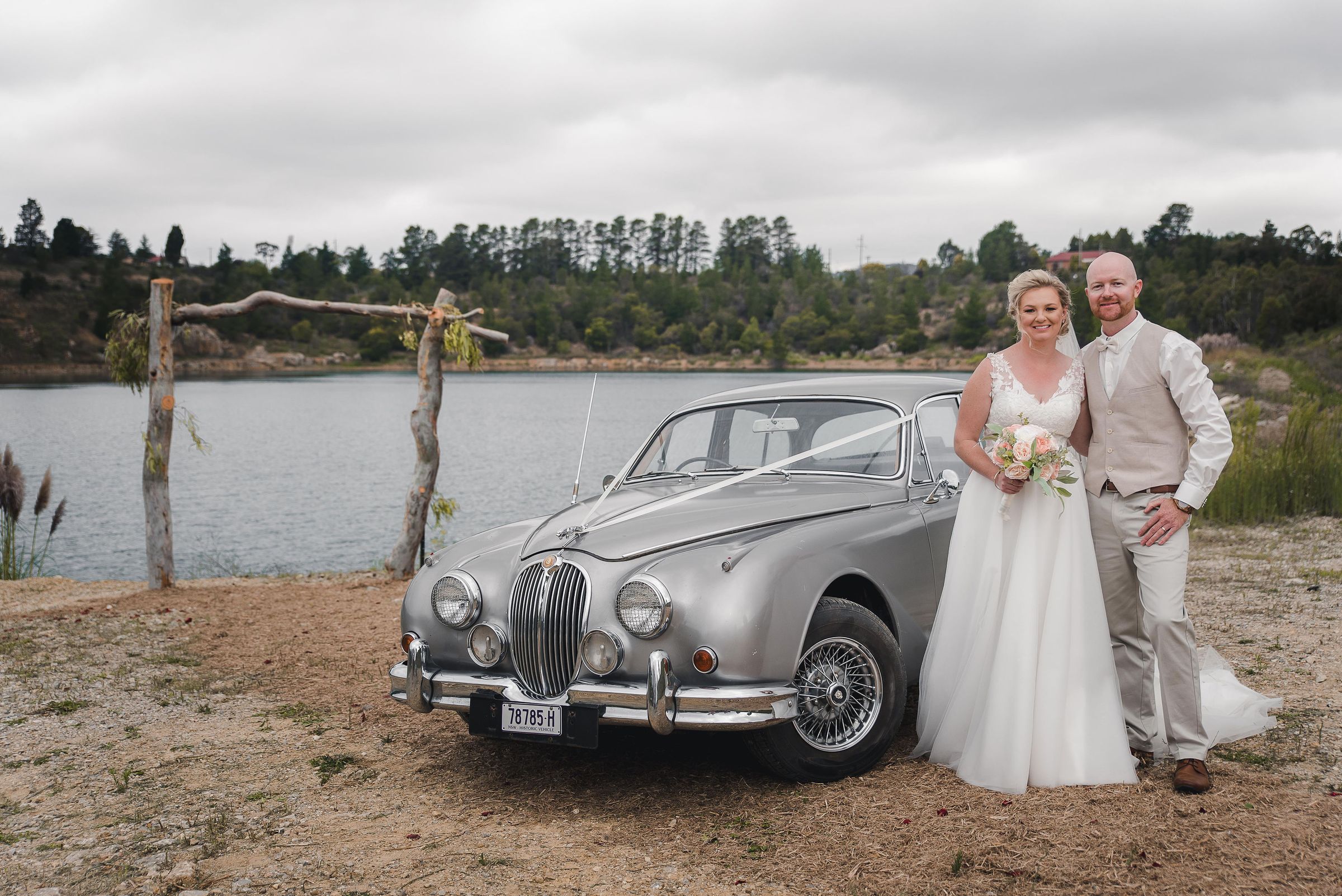 A bride and groom beside a vintage Jaguar at the lake