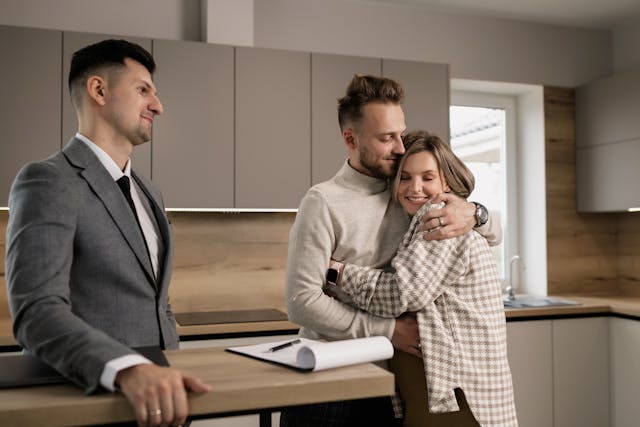 A couple hugging and a real estate agent standing beside them, smiling