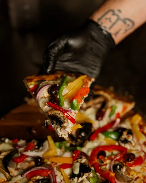 Slice of vegetarian pizza with mushrooms, capsicum and olives lifted from the board