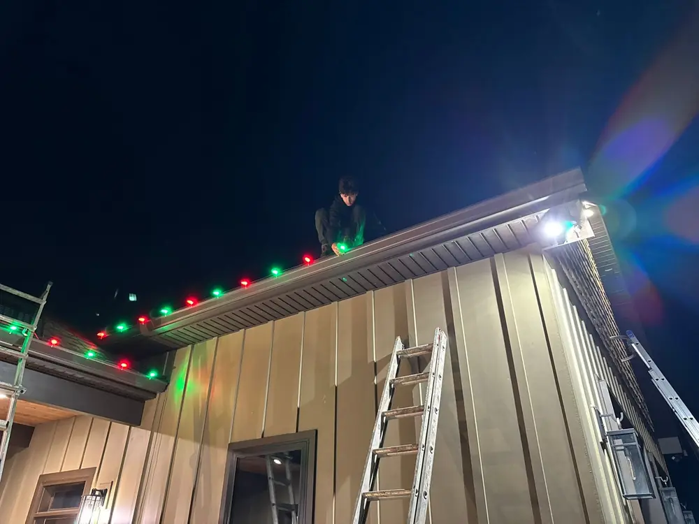 Wash Wizard installer hanging Christmas lights on a roof at night