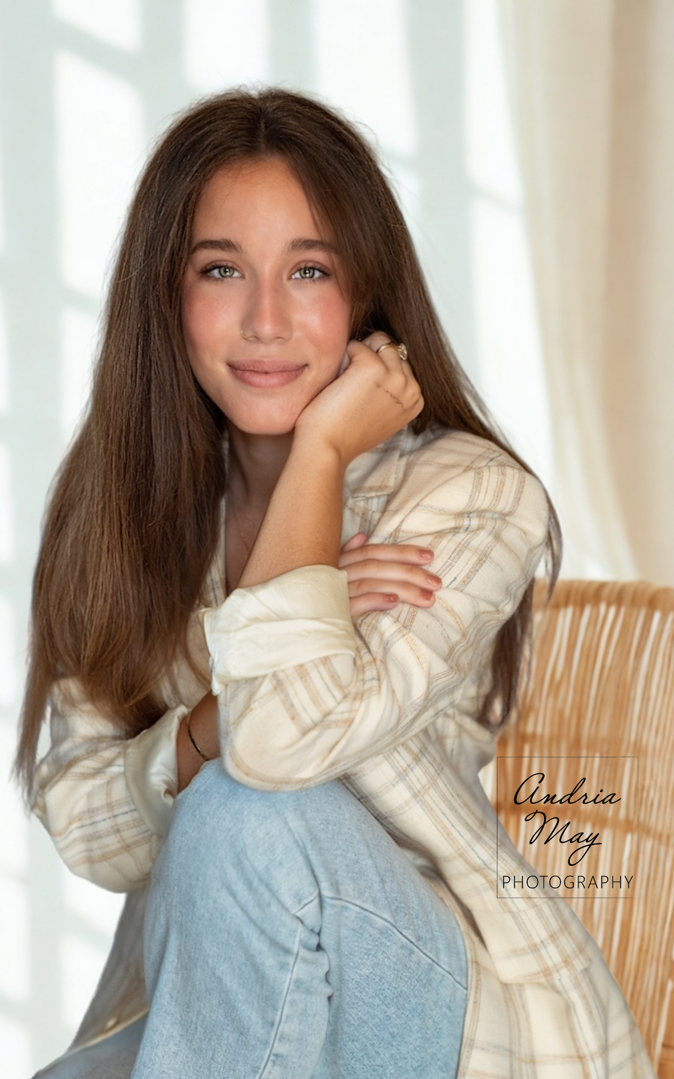 Indoor senior portrait of a high school senior seated in a wicker chair with natural window light, photographed in Gilbert, Arizona by Andria May Photography.