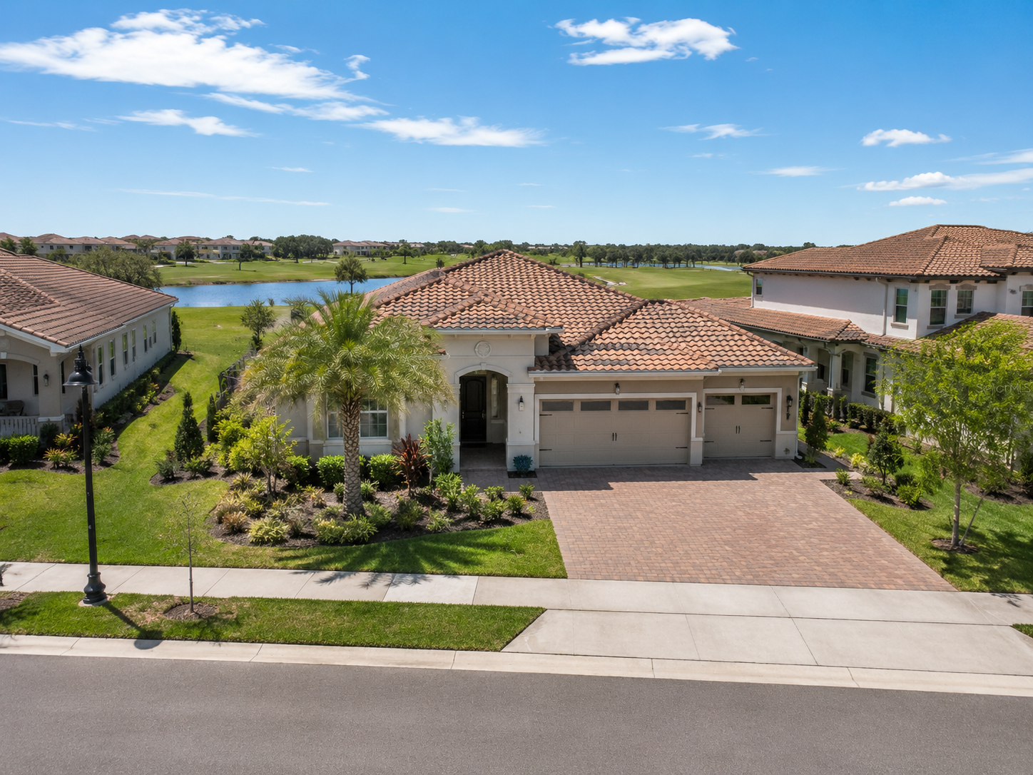 Eagle Creek Lake Nona home overlooking the golf course and water, featuring a tile roof, paver driveway, tropical landscaping, and Central Florida community views.
