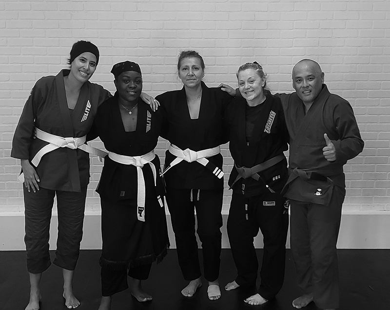 A group of diverse adult students wearing gis and white belts standing together arm-in-arm at a Brazilian Jiu-Jitsu gym. A group of diverse adult students wearing gis and white belts standing together arm-in-arm at a Brazilian Jiu-Jitsu gym.