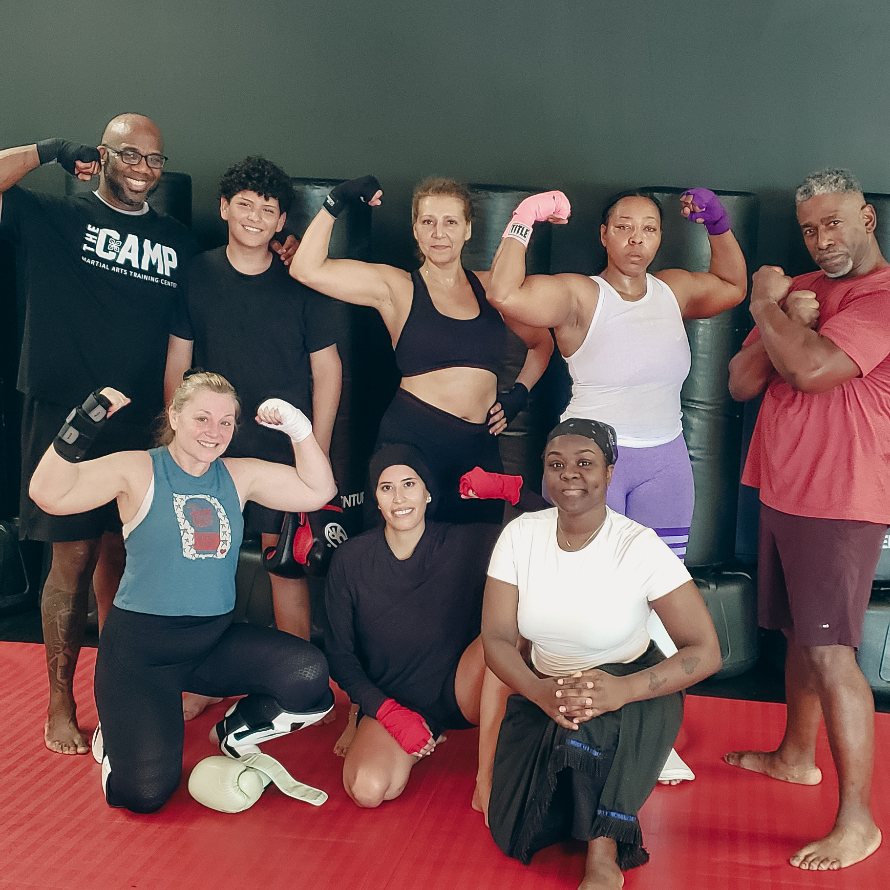A diverse group of individuals flexing muscles in a martial arts training setting A diverse group of individuals flexing muscles in a martial arts training setting