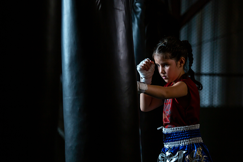Young girl with wrapped hands focusing on heavy bag striking mechanics in youth martial arts training