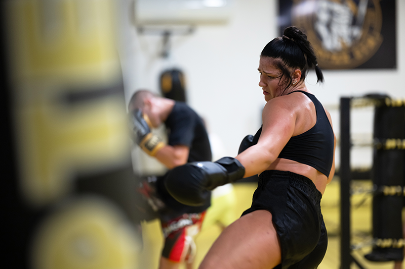 Female athlete executing a Muay Thai roundhouse kick on a heavy bag in a gym class Female athlete executing a Muay Thai roundhouse kick on a heavy bag in a gym class