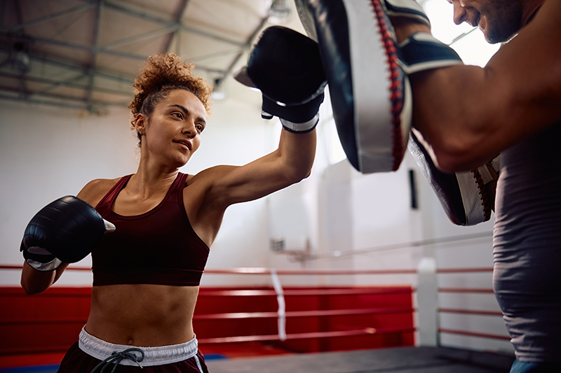 Female athlete landing a straight punch on focus mitts held by a coach in a boxing ring Female athlete landing a straight punch on focus mitts held by a coach in a boxing ring