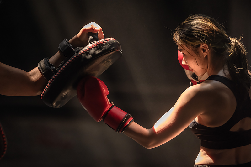 Woman throwing a boxing uppercut punch into a focus mitt during beginner striking drills Woman throwing a boxing uppercut punch into a focus mitt during beginner striking drills