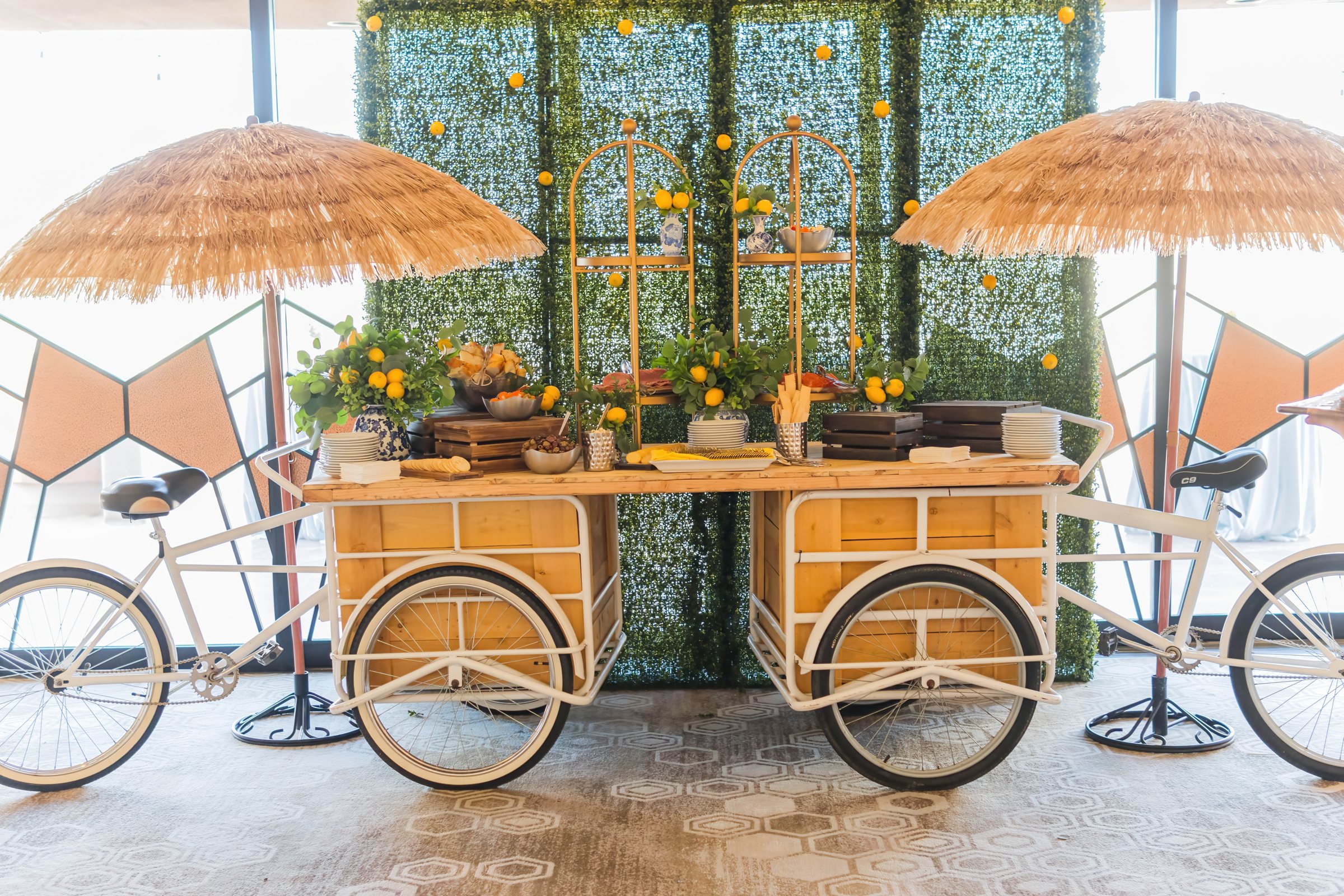 Bicycle cart grazing station with raffia umbrellas, lemons, and a hedge wall