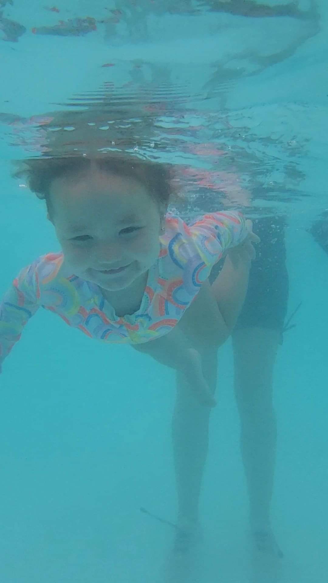 Child underwater in rainbow swimsuit at AquaSquad Swim