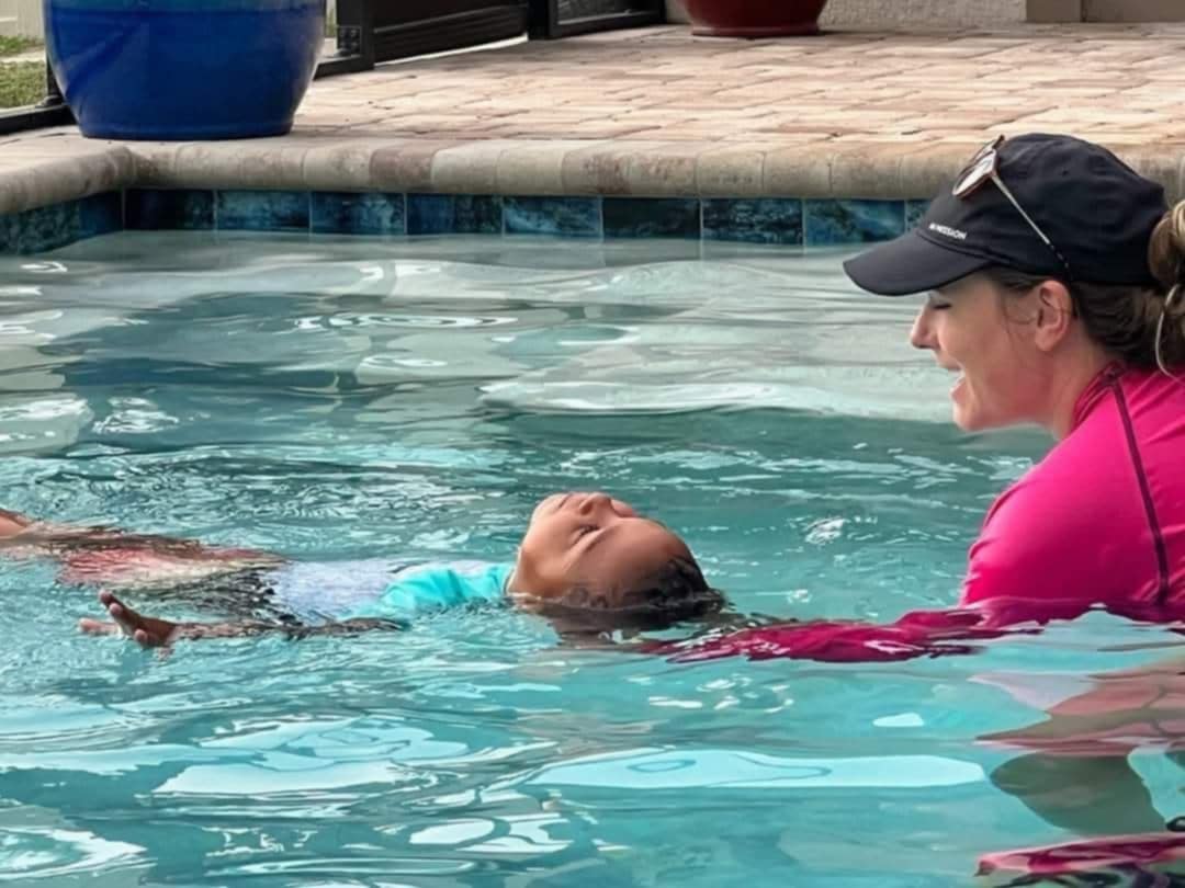 AquaSquad instructor smiling at child floating on back in pool