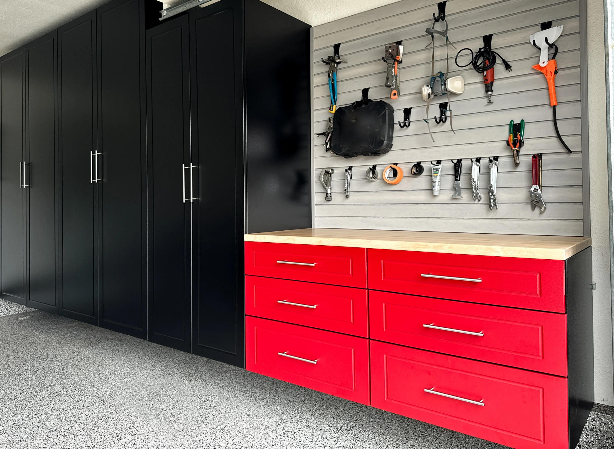 Custom black full-height garage cabinets with red drawer workbench, butcher block countertop, and slatwall tool organization