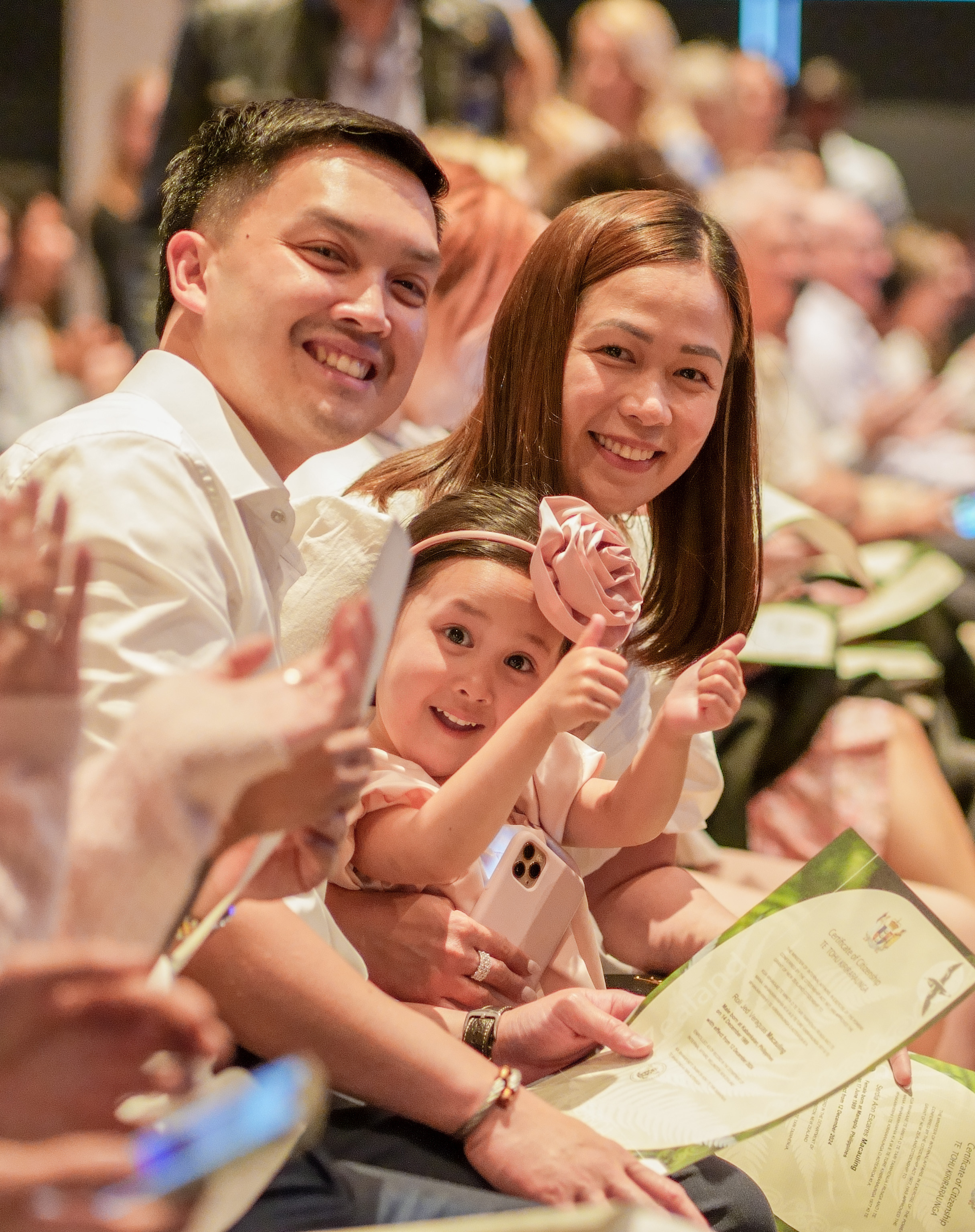 A girl with her parents, holding her graduation certificate