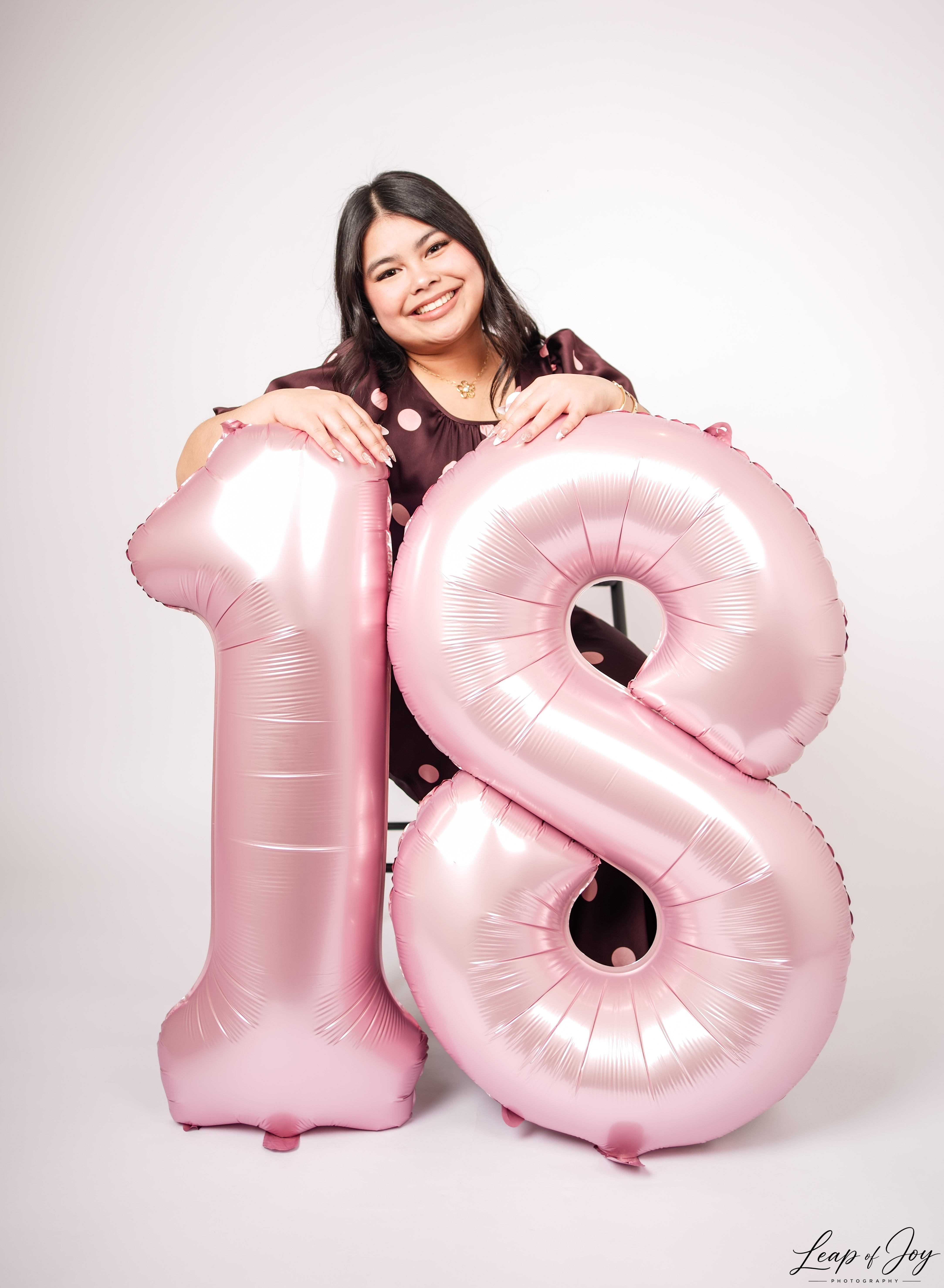 A young woman beside giant eighteenth birthday balloons