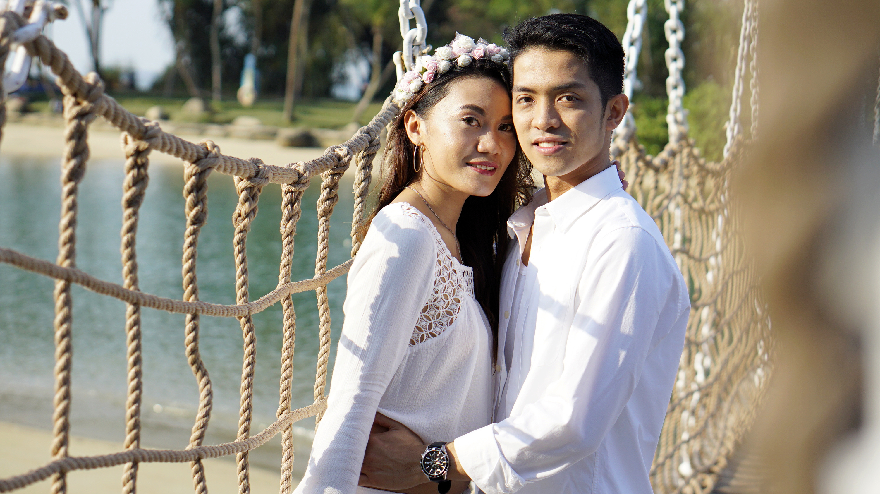 An engaged couple photographed by a rope bridge on the beach