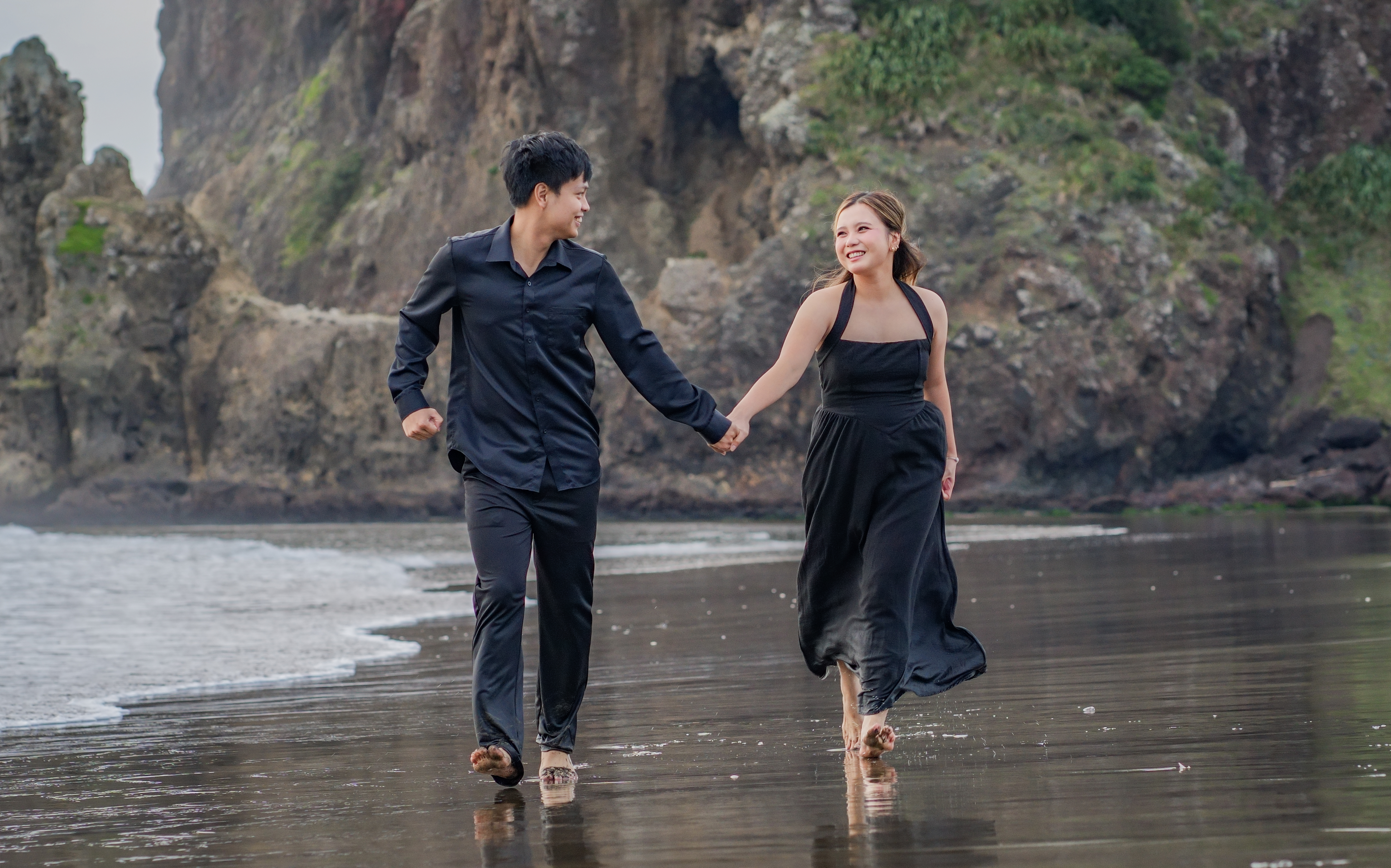 A couple walking barefoot along a black sand beach