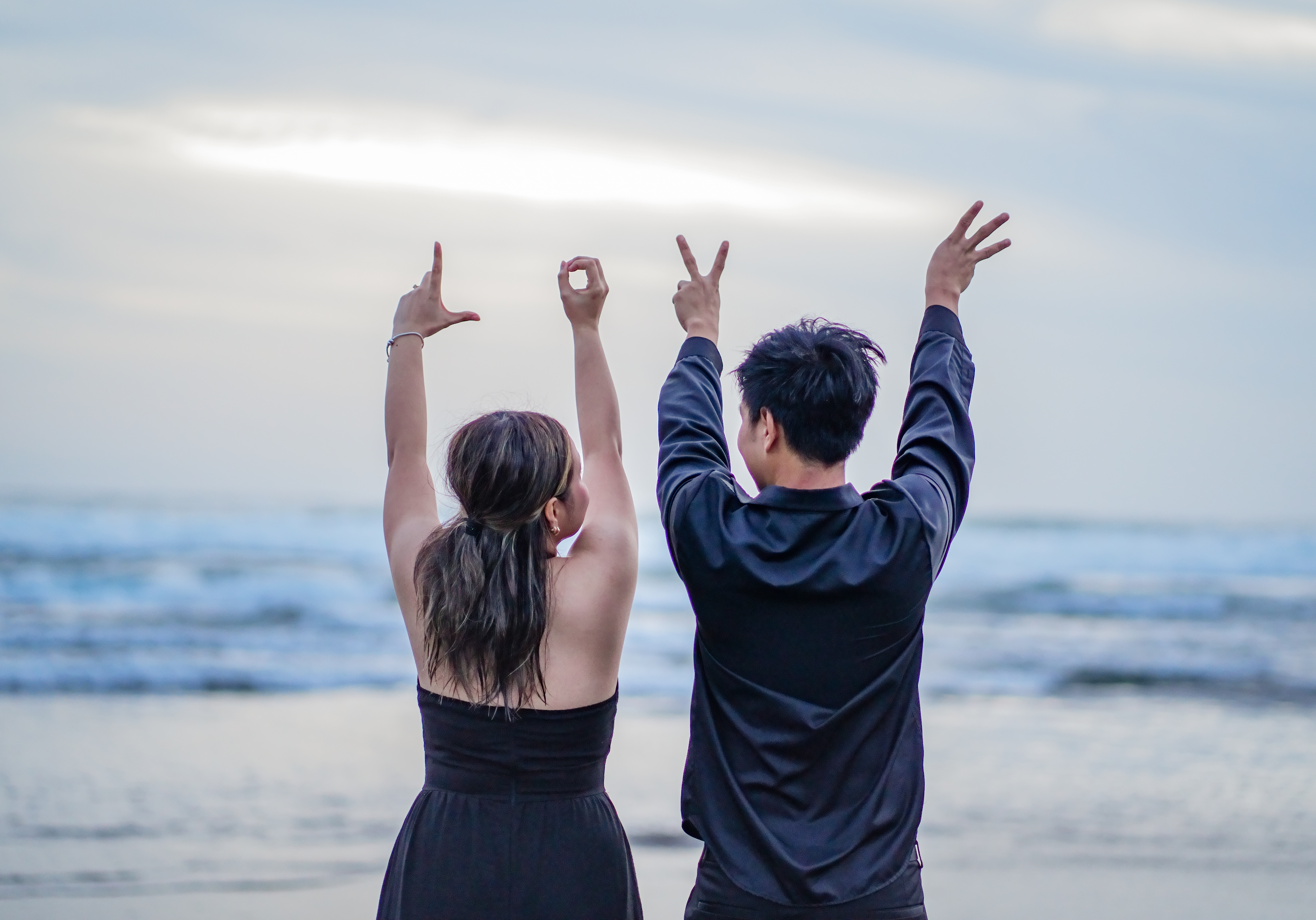 A newly engaged couple raising the ring at the water’s edge