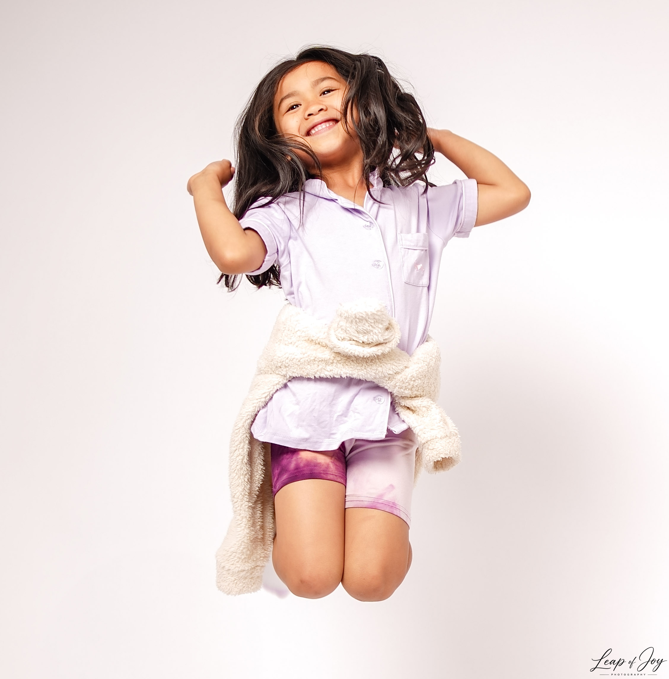 A young girl leaping mid-air in the studio, laughing