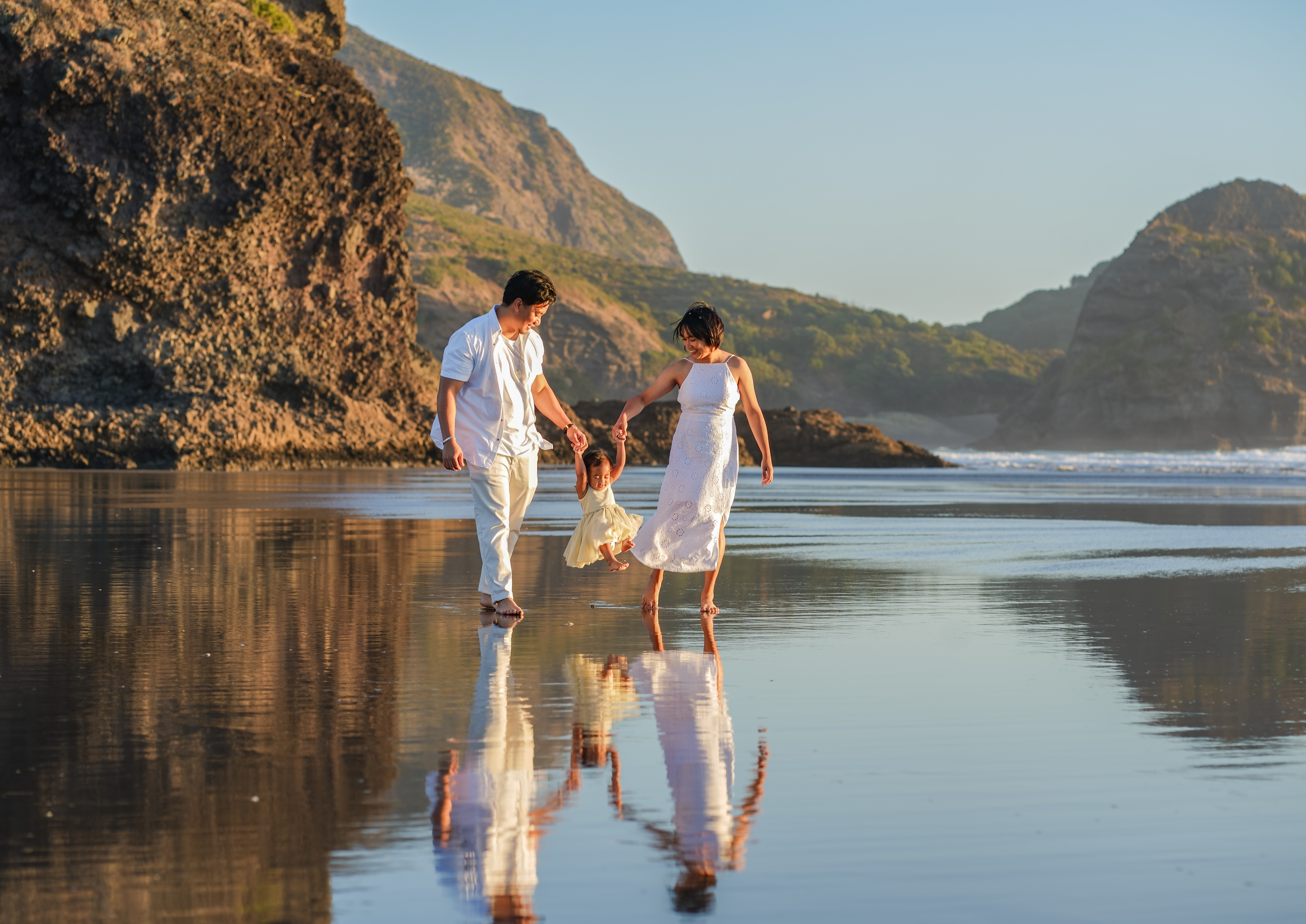 A family walking barefoot on an Auckland beach at golden hour